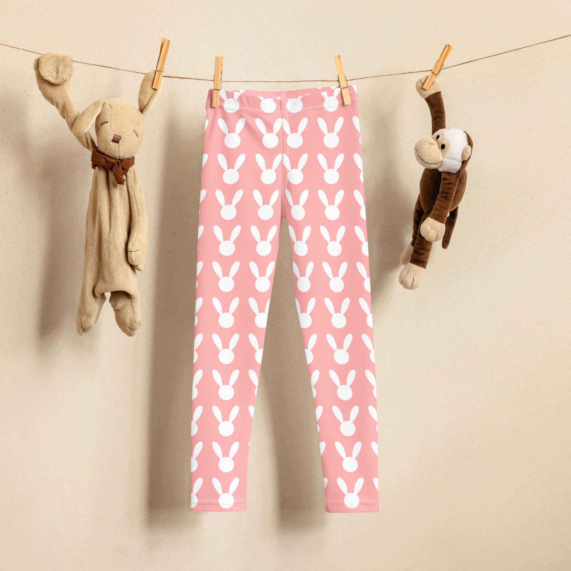 Girls pink buttery soft leggings with white bunny pattern hanging on a clothesline between two stuffed animals
