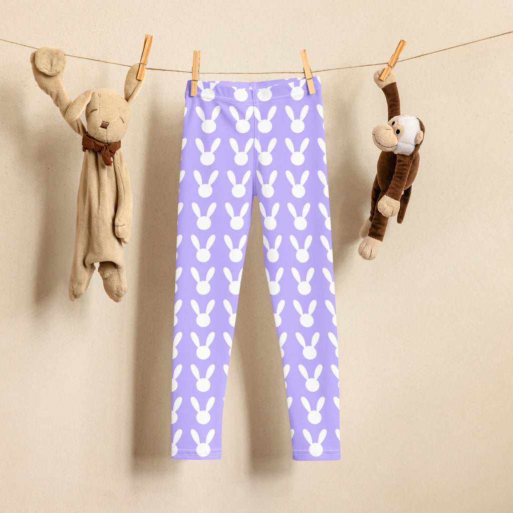 Girls purple buttery soft leggings with white bunny pattern hanging on clothesline between stuffed animals