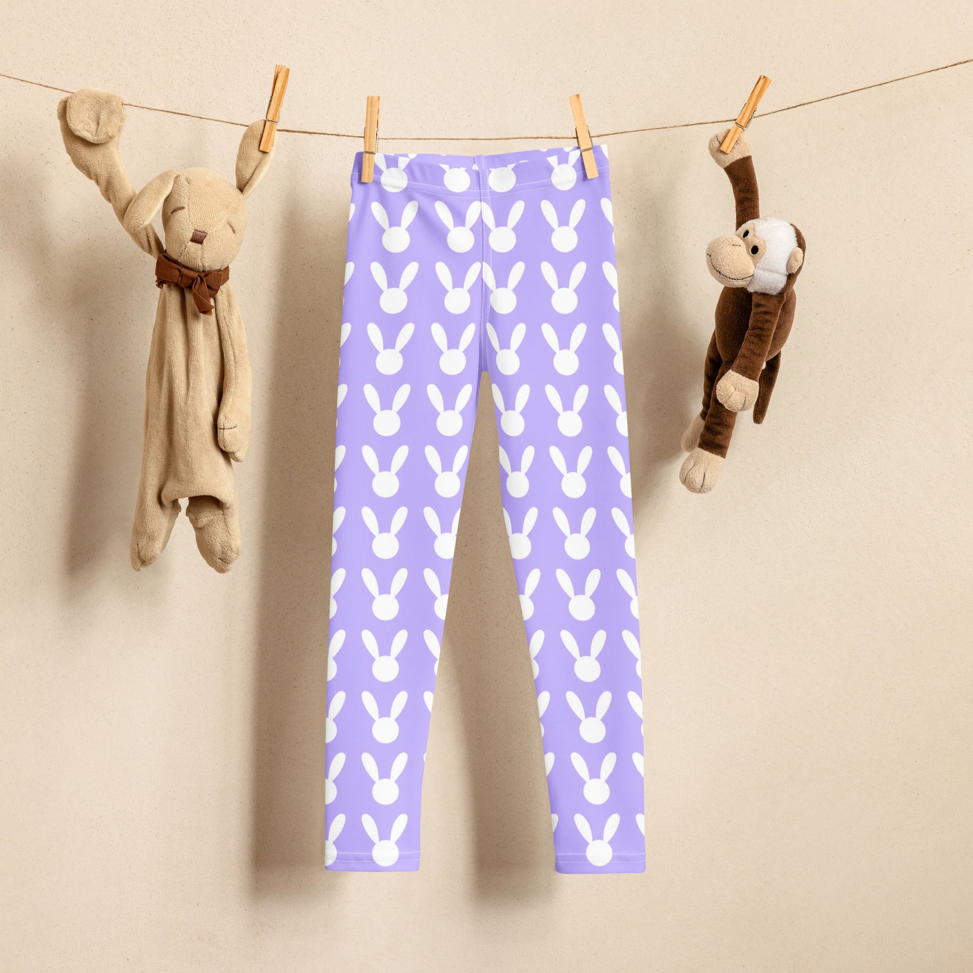 Girls purple buttery soft leggings with white bunny pattern hanging on clothesline between stuffed animals