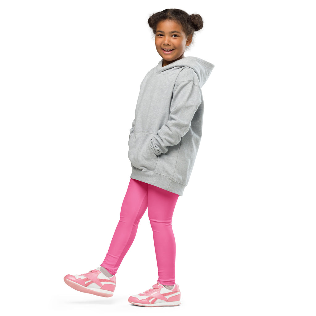 Smiling girl in a gray hoodie and pink kids leggings, standing against white background
