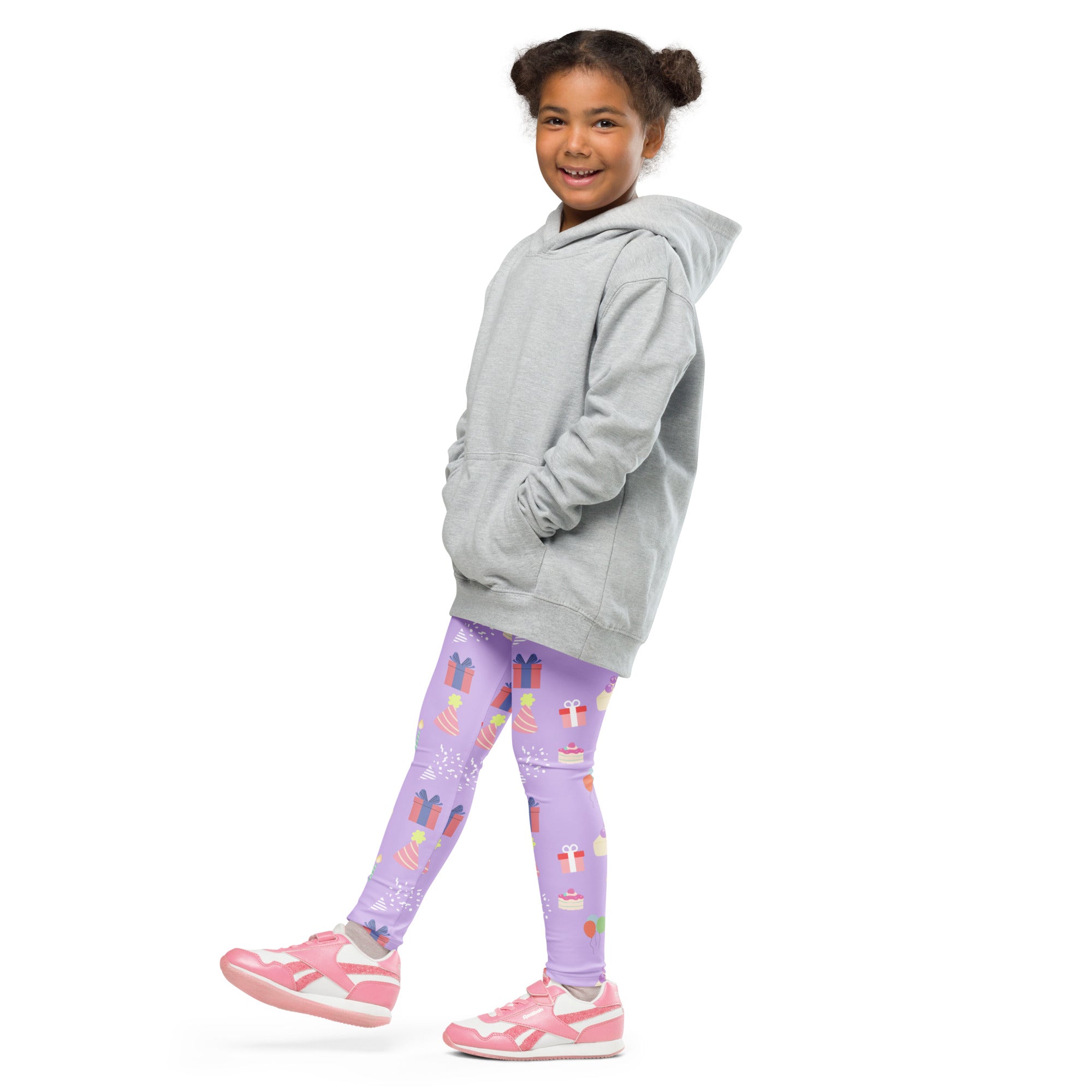A young girl wearing girls birthday buttery soft leggings in purple with colorful gift patterns and pink athletic shoes