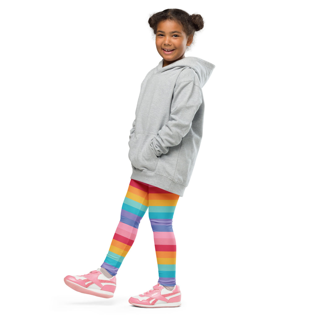 A child wearing girls bright rainbow striped buttery soft leggings in rainbow colors with pink sneakers and a gray hoodie