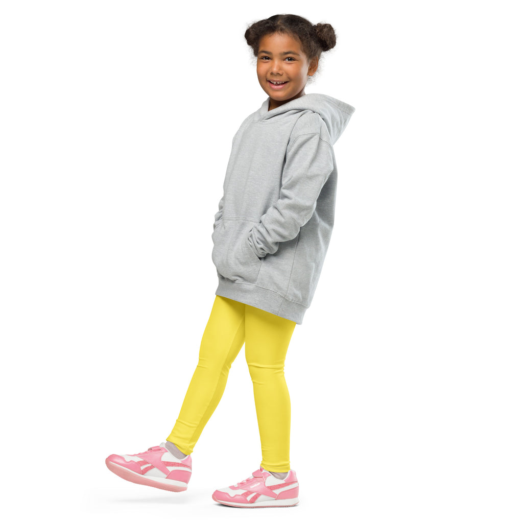 A young girl wearing kids buttery soft yellow leggings paired with a light gray hooded sweatshirt