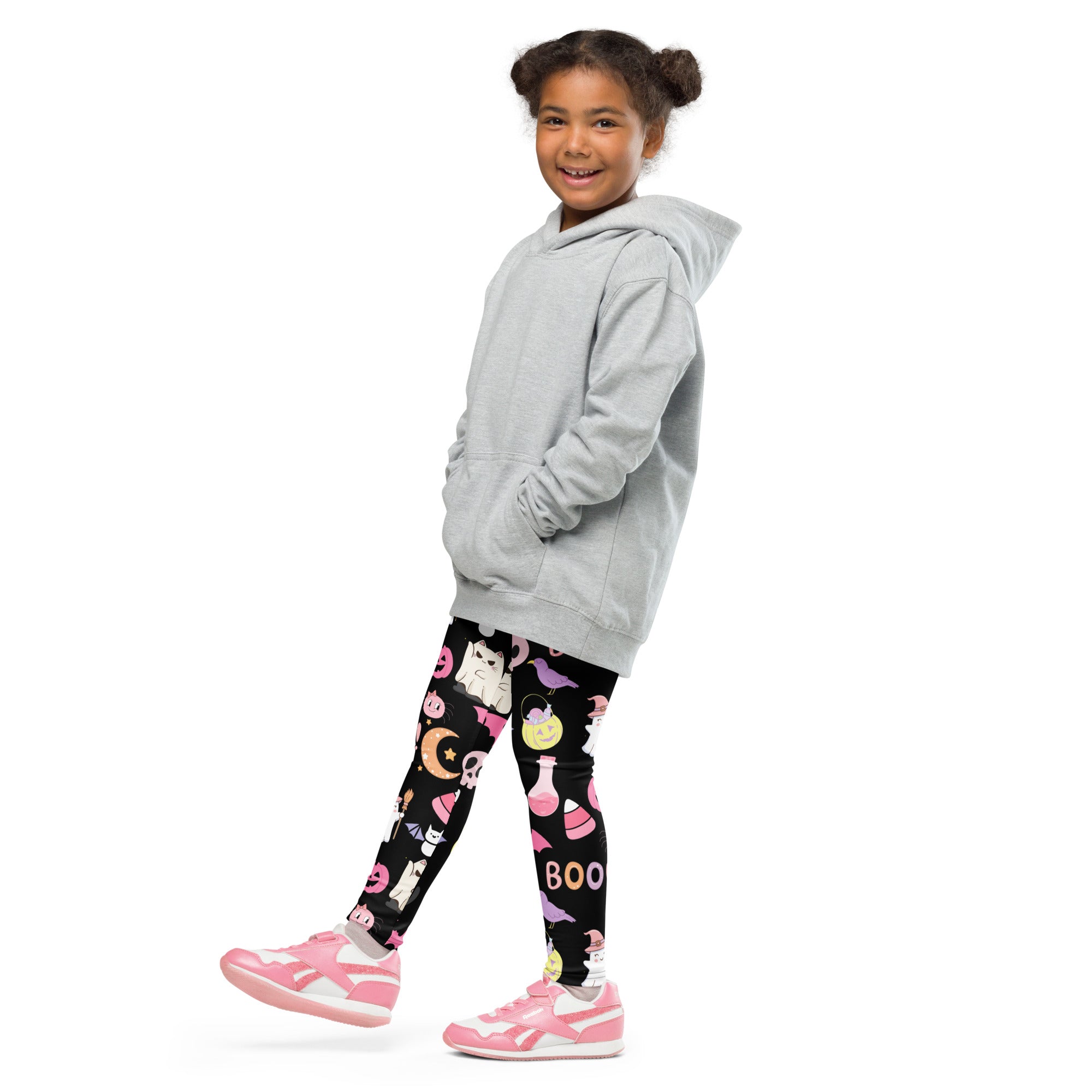 A young girl wearing girls cute halloween buttery soft leggings in black with pink graphics and a light gray hooded sweatshirt