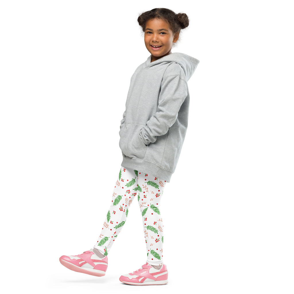 A young girl wears kids holly and pine buttery soft Christmas leggings with green leaf red berry patterns and pink shoes