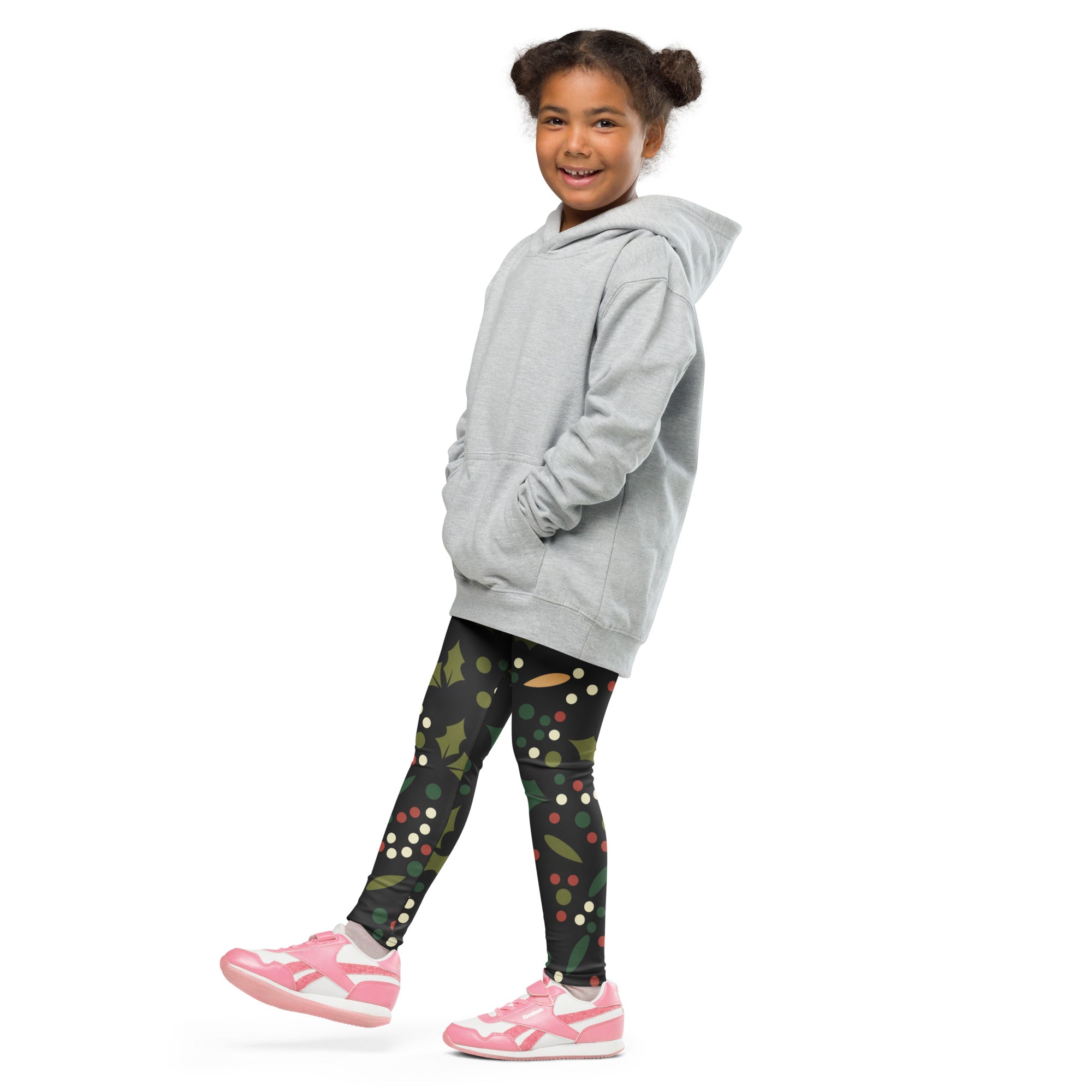 A young girl wearing kids holiday holly buttery soft leggings in festive pattern with pink sneakers and gray hoodie
