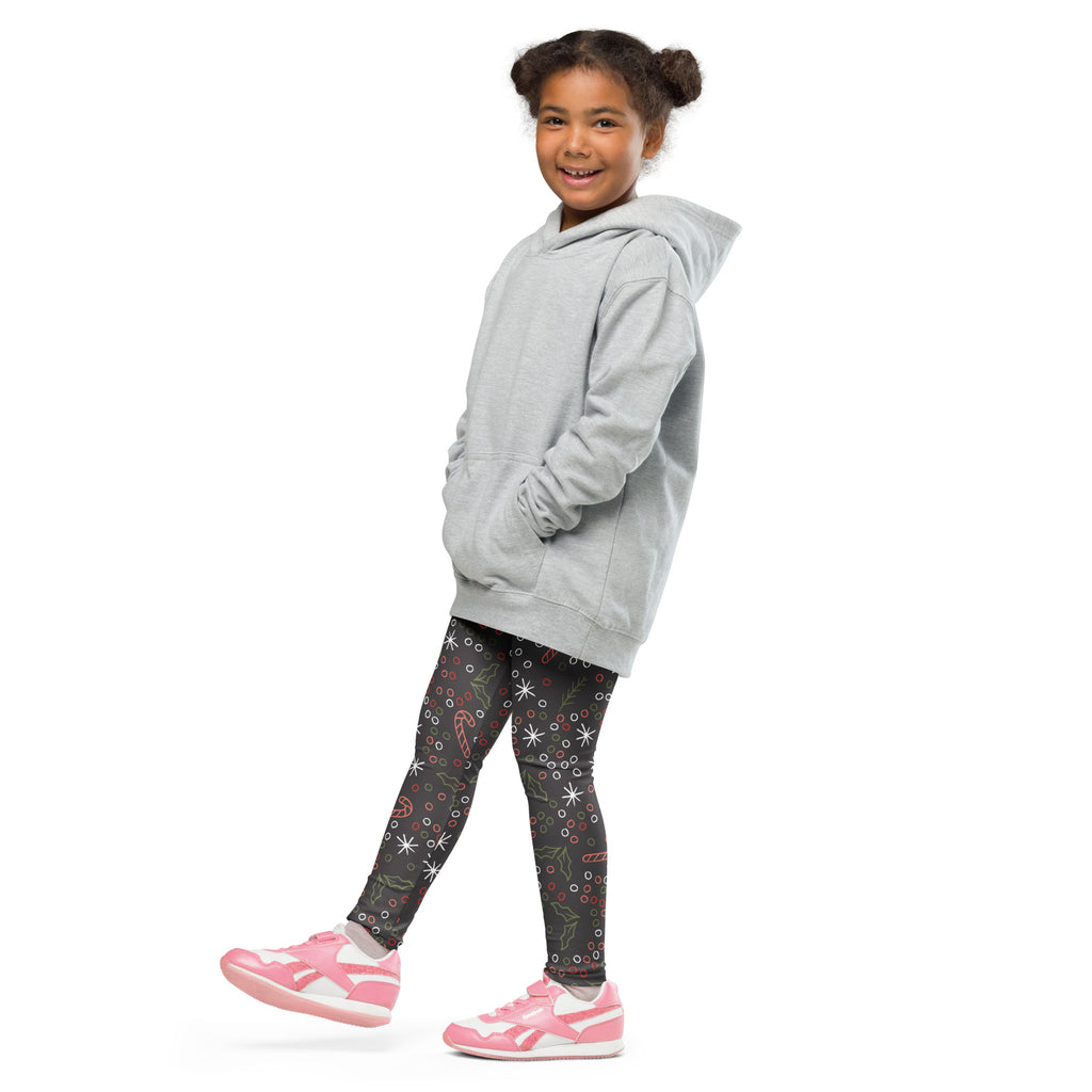 A child wearing kids Christmas candy canes and holly leaves buttery soft leggings with a light gray hooded sweatshirt