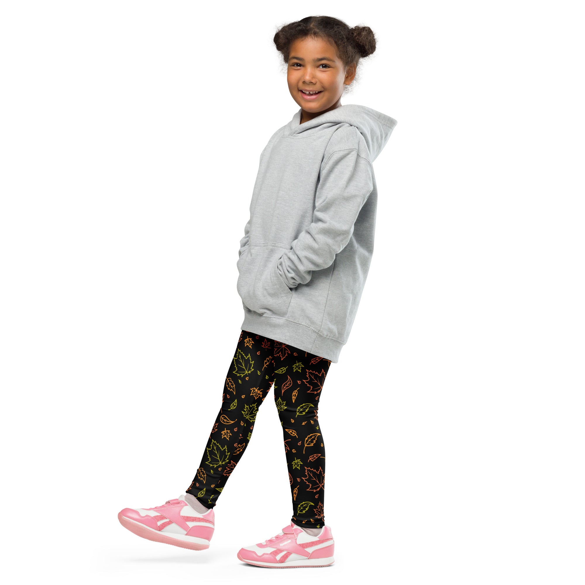 A young girl wearing kids fall leaf buttery soft leggings with colorful leaf patterns in black paired with pink shoes