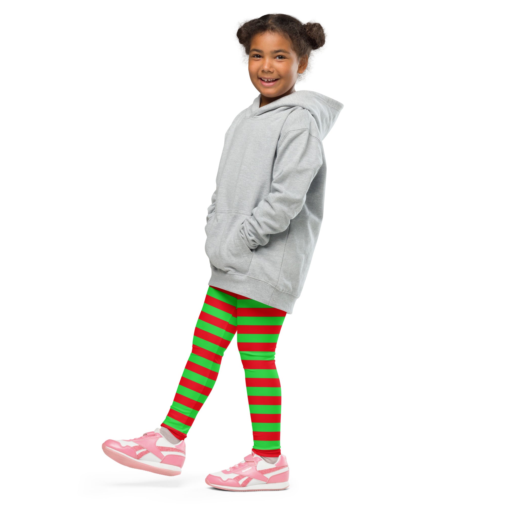 A young girl wearing buttery soft kids red and green striped Christmas leggings with pink sneakers and gray hoodie