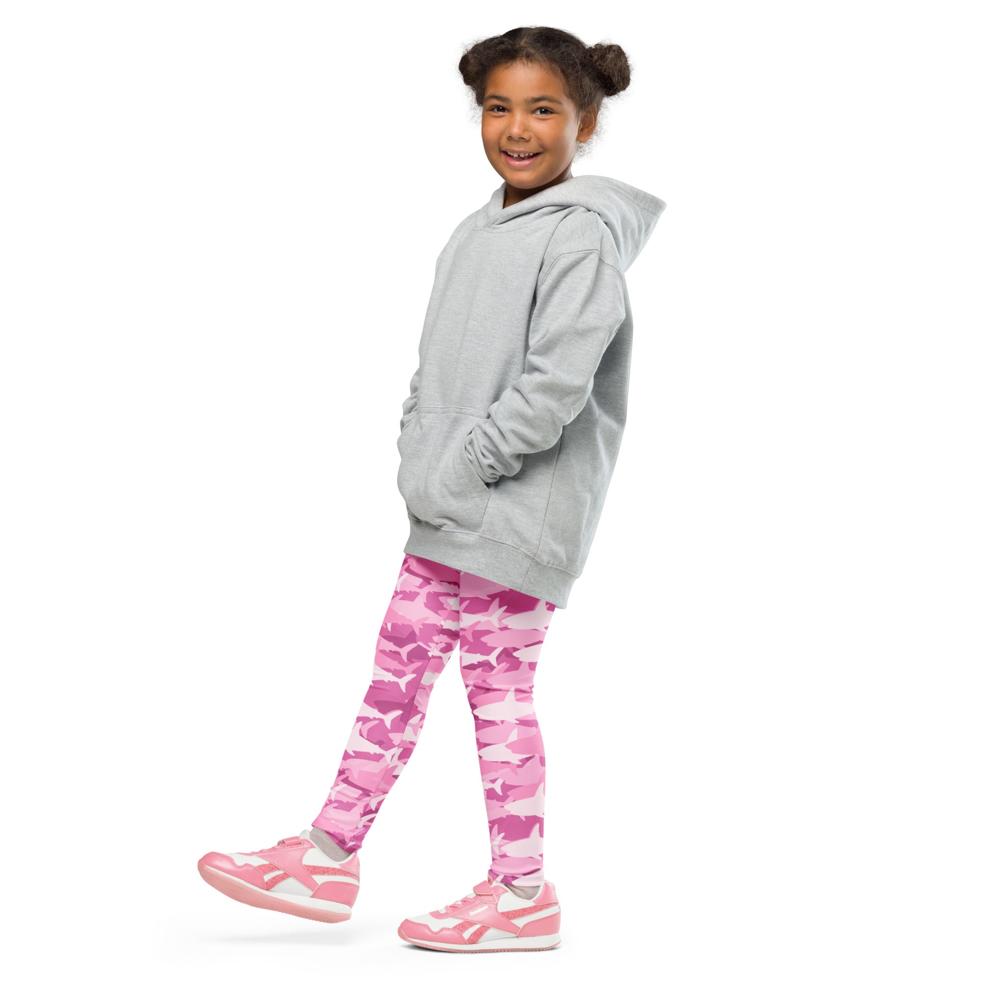 A child wearing girls pink shark buttery soft leggings with pink camouflage and shark patterns paired with matching sneakers