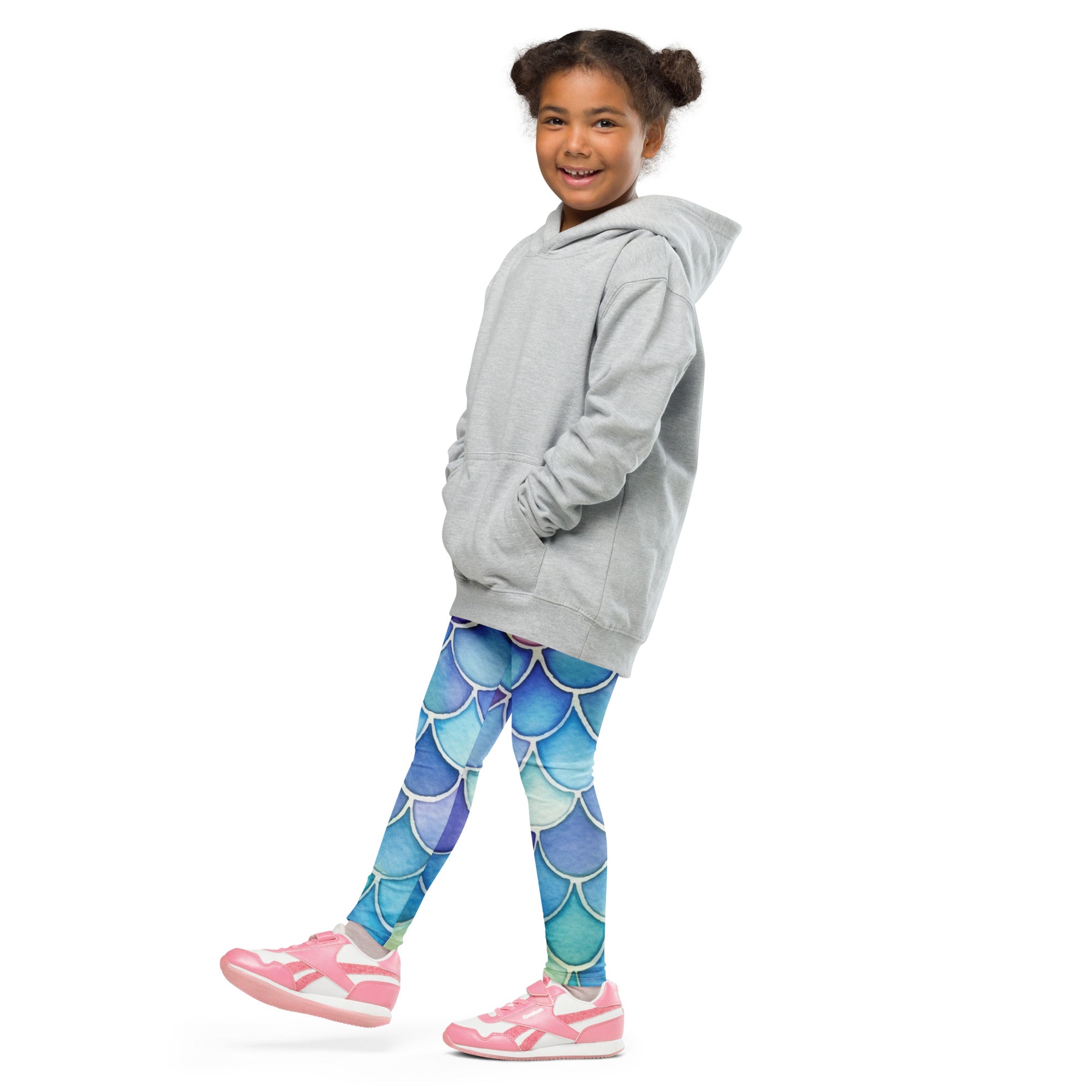 A child wearing girls watercolor mermaid buttery soft leggings in vibrant blue mermaid scale pattern with pink sneakers