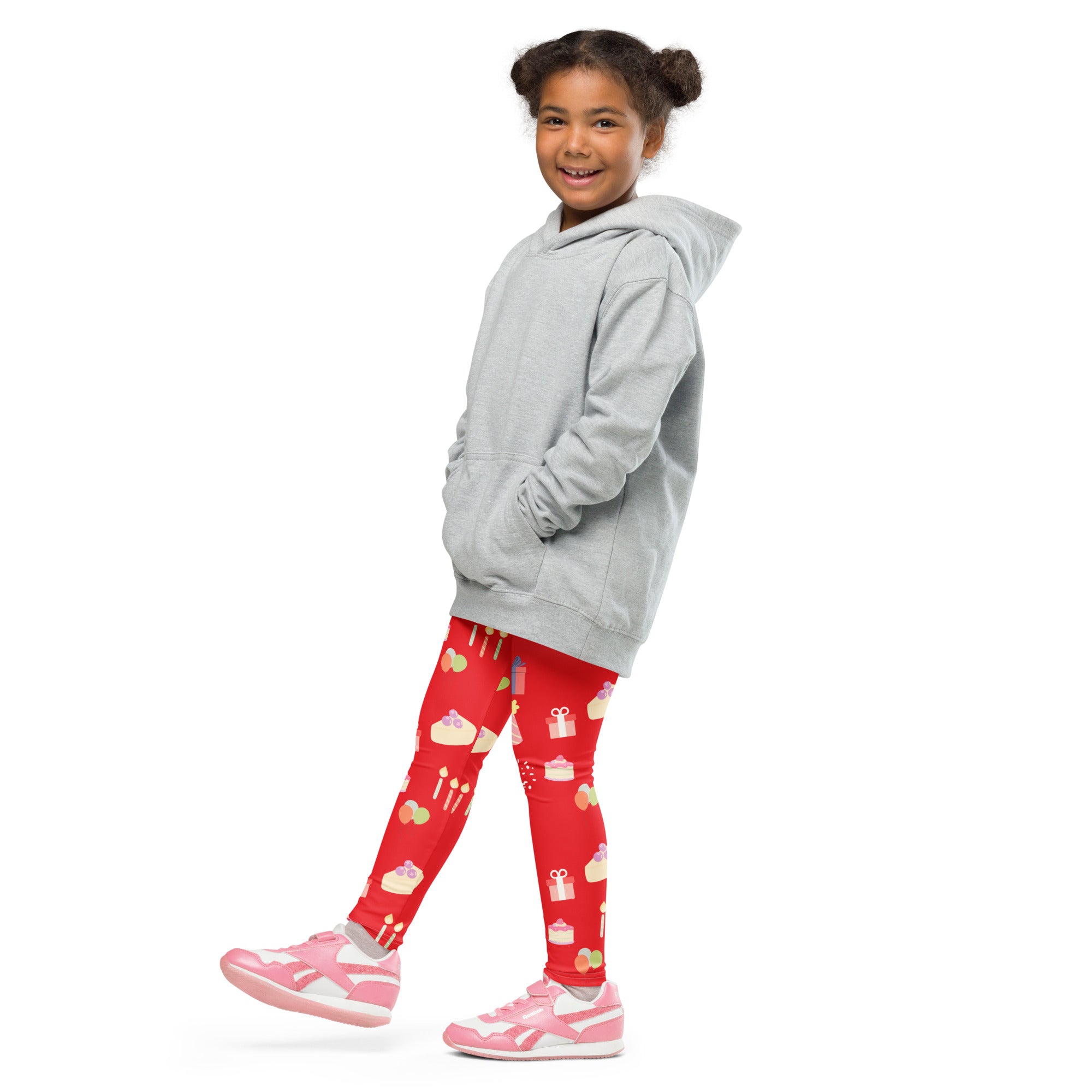 A young girl wearing kids red birthday pattern buttery soft leggings with playful cake and gift design and a gray hoodie