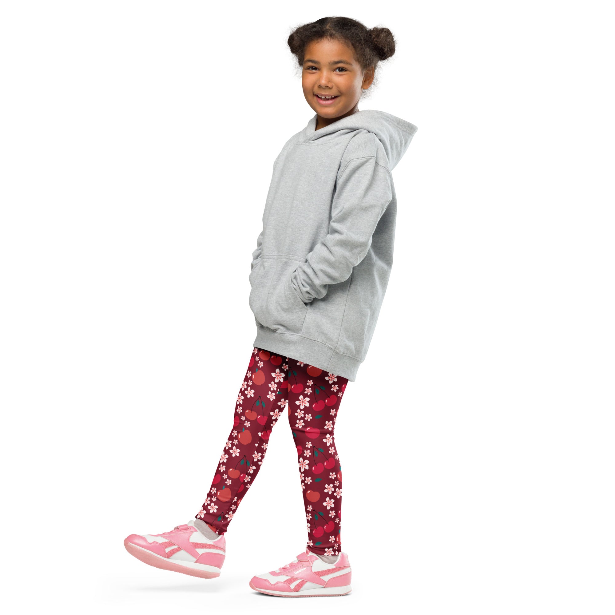 A young girl wearing girls cherry blossom print buttery soft red leggings with pink sneakers and a gray hoodie