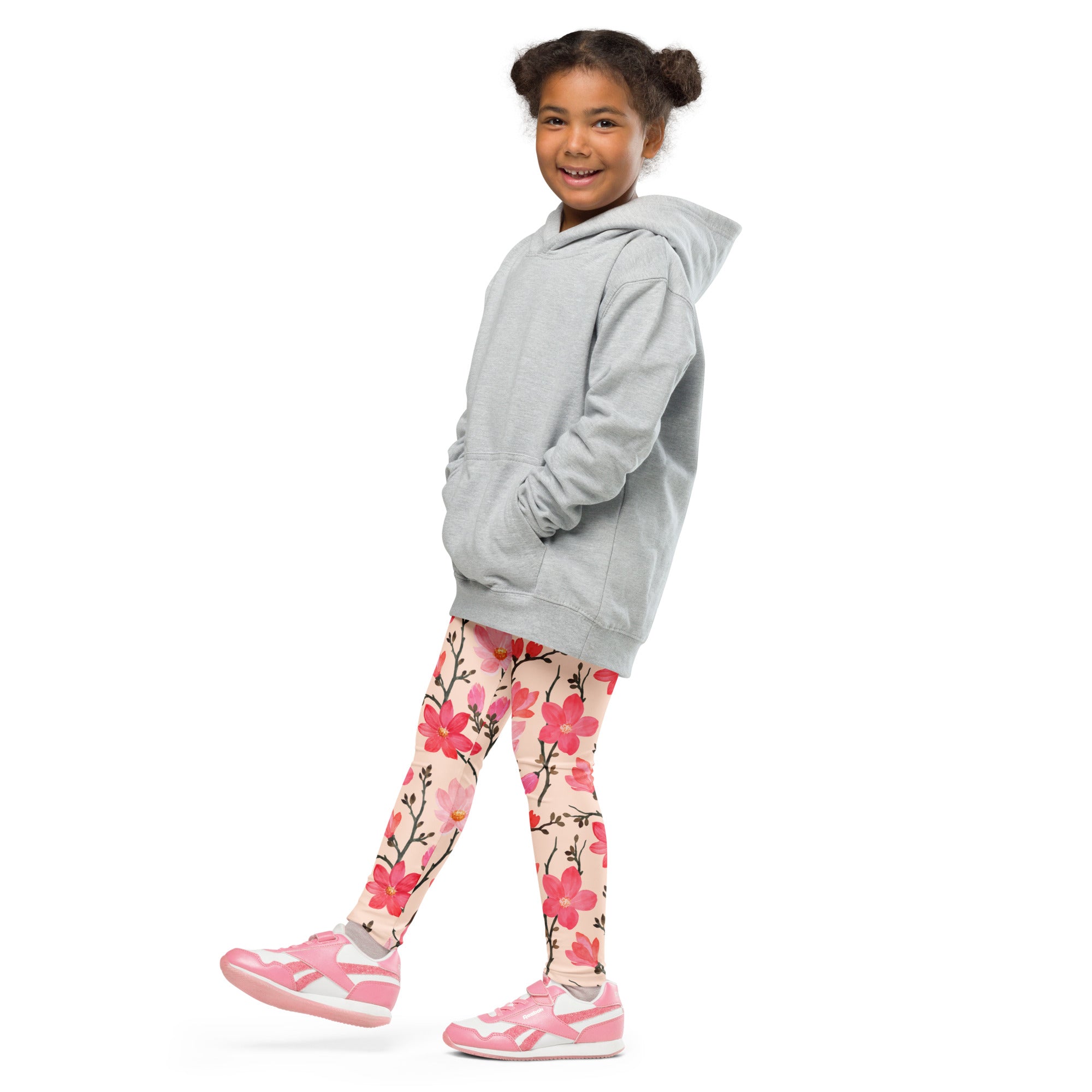 A young girl wearing girls pink watercolor floral buttery soft leggings in pink with a light gray hooded sweatshirt