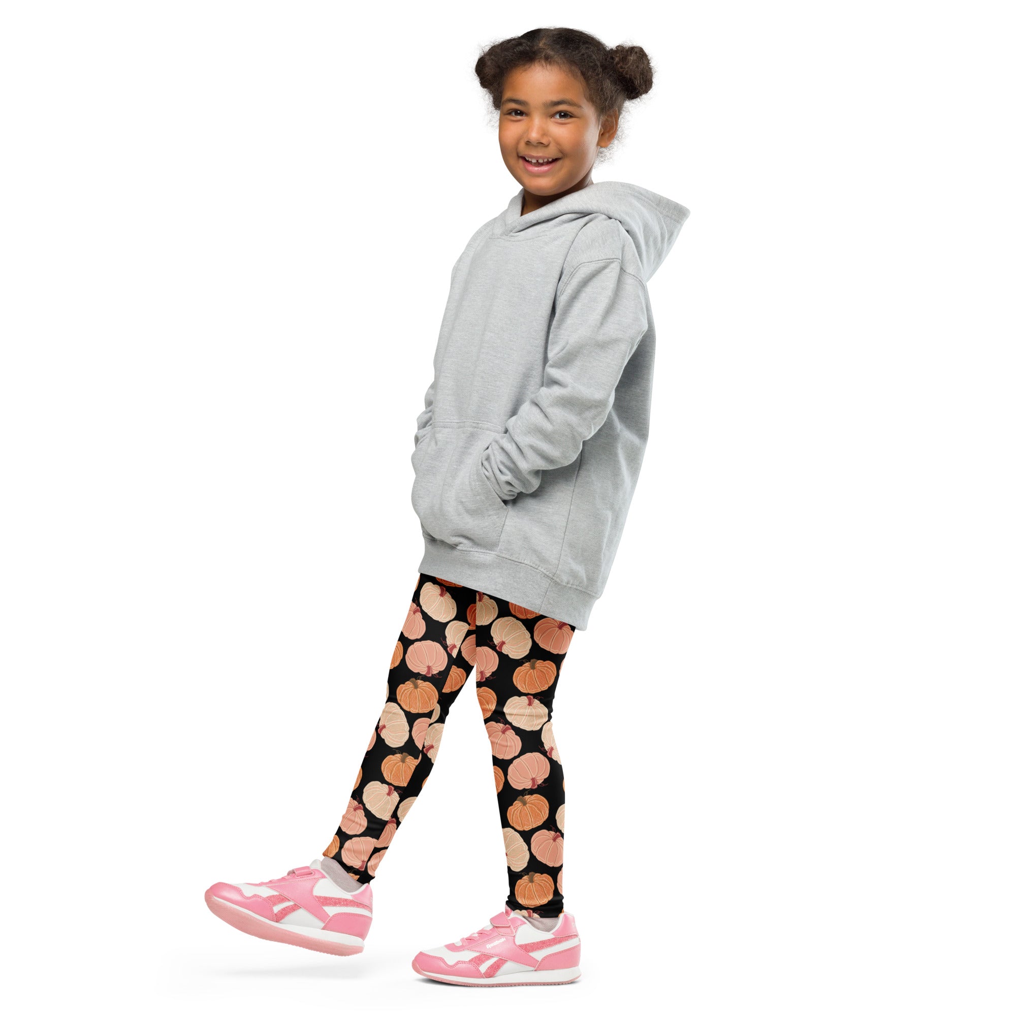 A young girl wearing kids fall pumpkins buttery soft black leggings with orange pumpkin prints and a gray hooded sweatshirt
