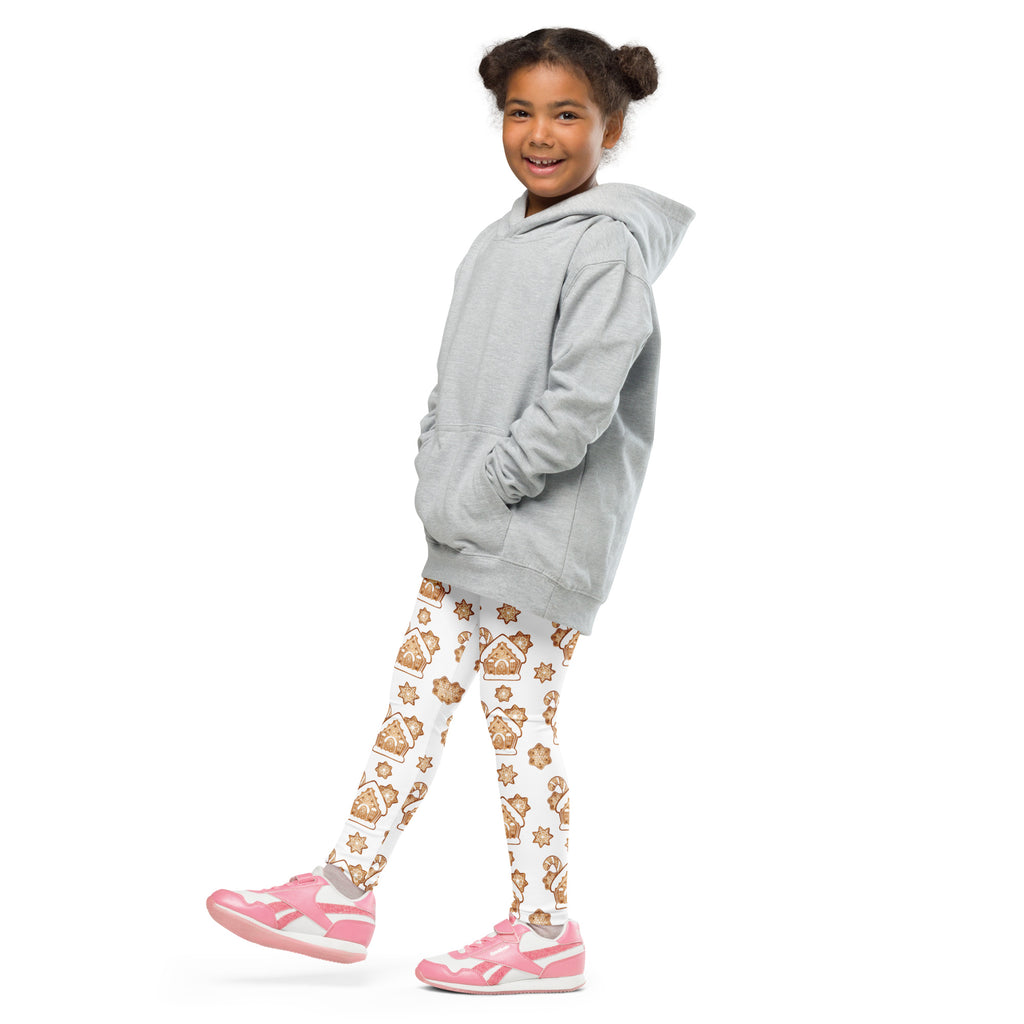 A young girl wearing kids gingerbread house Christmas buttery soft light gray hooded sweatshirt and white leggings with brown patterns