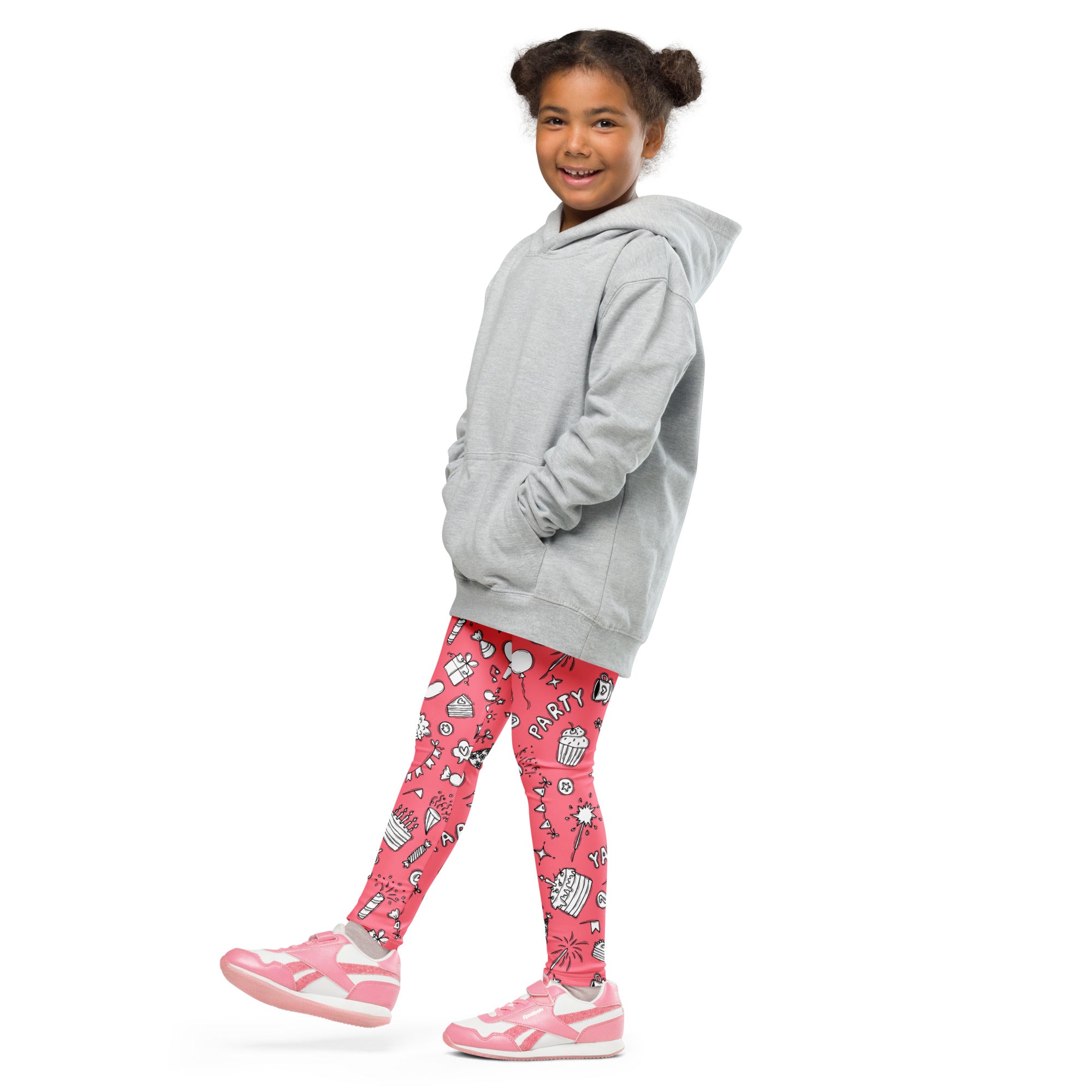 A young girl wearing girls pink birthday party buttery soft leggings with playful party-themed illustrations and a gray hoodie