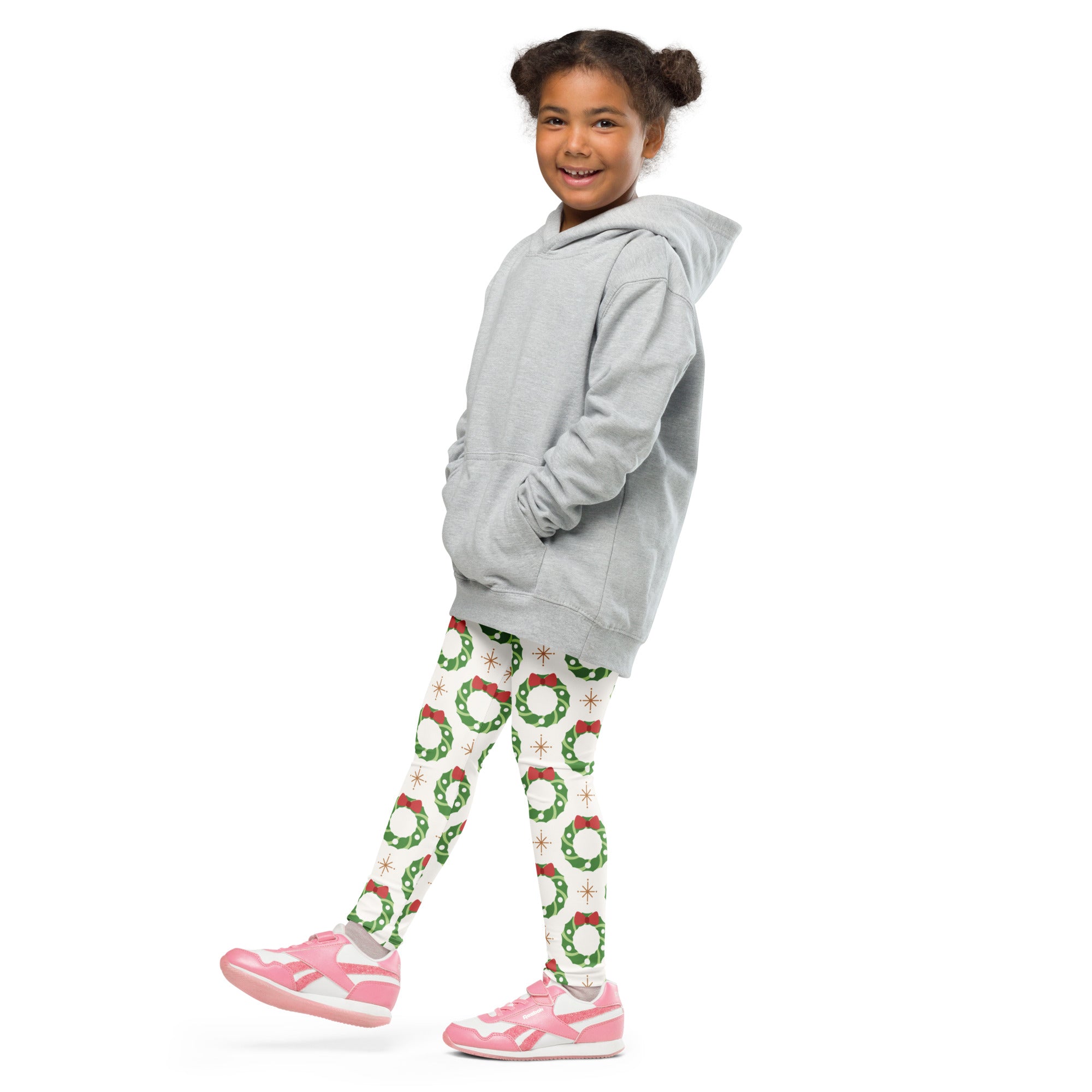 A young girl wearing kids holiday wreath buttery soft green leggings with festive pattern and pink sneakers