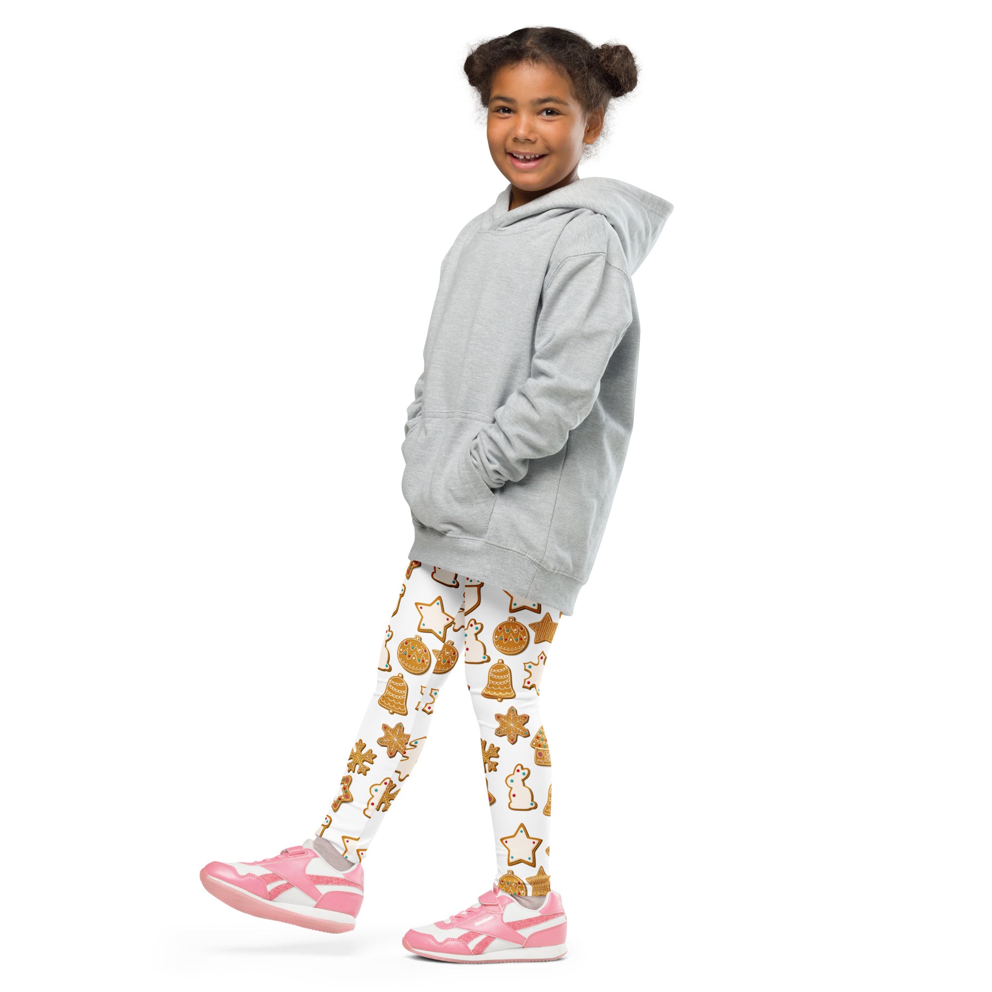 A young girl wearing buttery soft white leggings with golden holiday cookie patterns and a light gray hooded sweatshirt