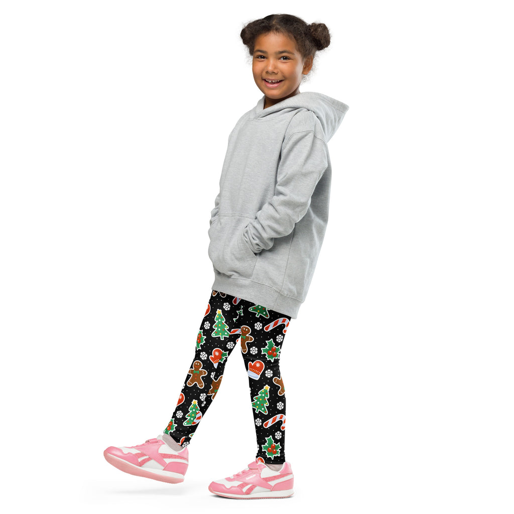 A child wearing light gray buttery soft kids gingerbread themed christmas leggings with festive holiday patterns