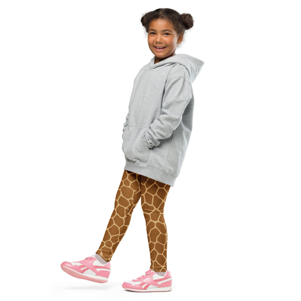 A young girl wearing kids giraffe print buttery soft brown leggings with a light gray hooded sweatshirt and pink sneakers