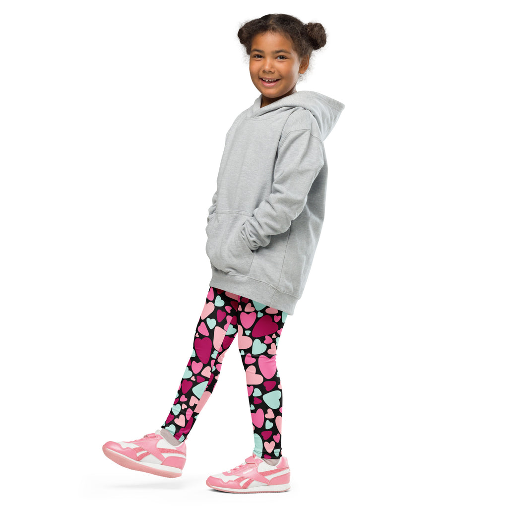 A young girl wearing multicolor heart buttery soft leggings with a light gray hooded sweatshirt and pink sneakers