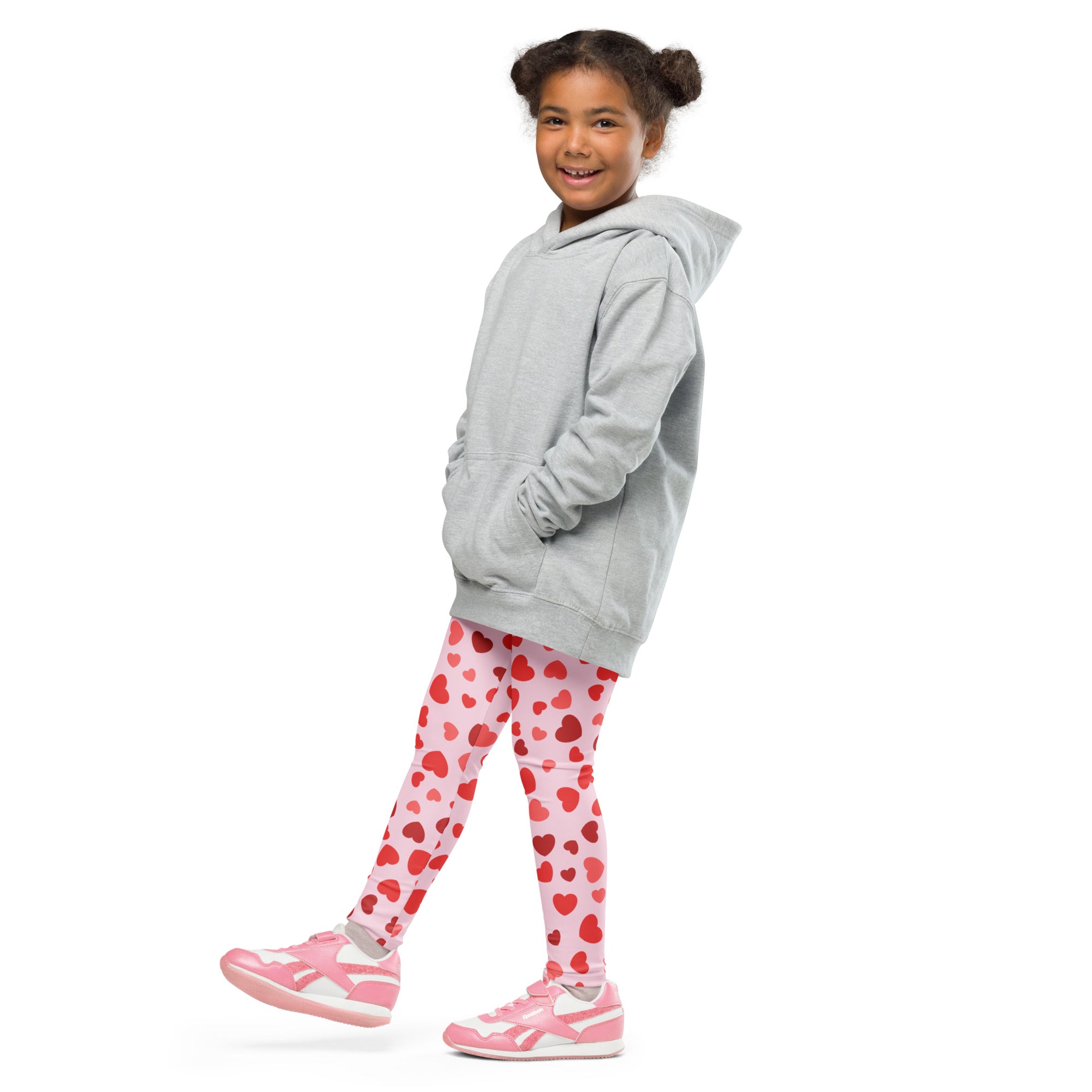 A young girl wearing girls Valentine’s Day pink heart buttery soft leggings with matching pink sneakers and gray hoodie