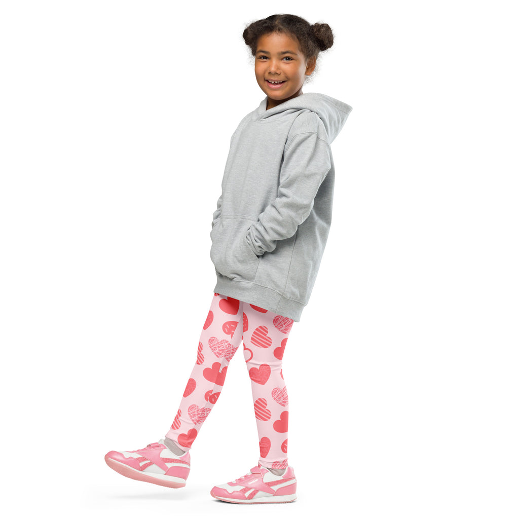 A young girl wearing buttery soft girls pink heart pattern leggings with matching pink sneakers and gray hoodie