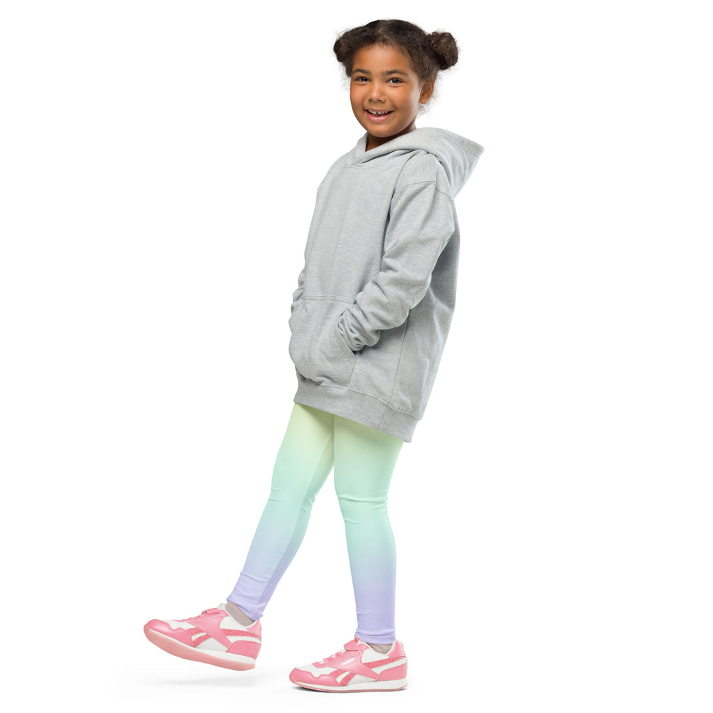 A child wearing girls pastel rainbow buttery soft leggings in a mint green to lavender gradient with a gray hooded sweatshirt
