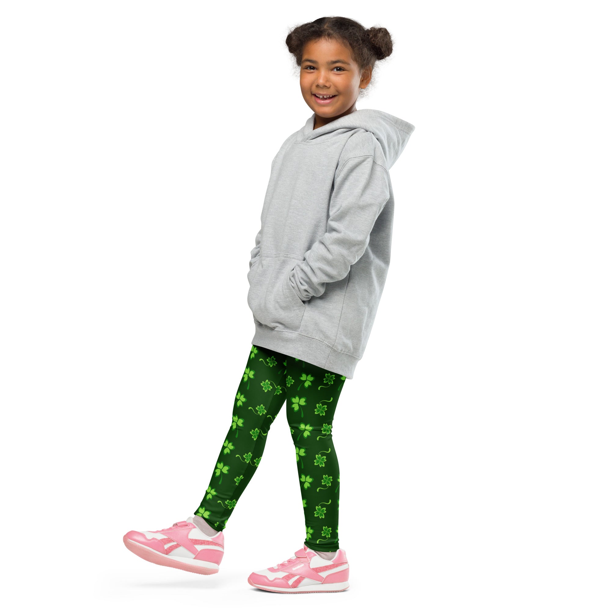 A child wearing girls green lucky clover buttery soft leggings with bright lime shamrock patterns and pink sneakers