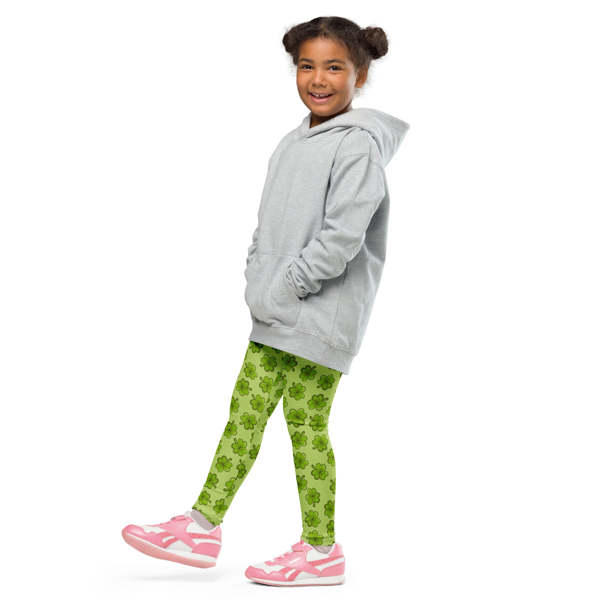 A young girl wearing lime green shamrock buttery soft leggings paired with a light gray hooded sweatshirt and pink shoes