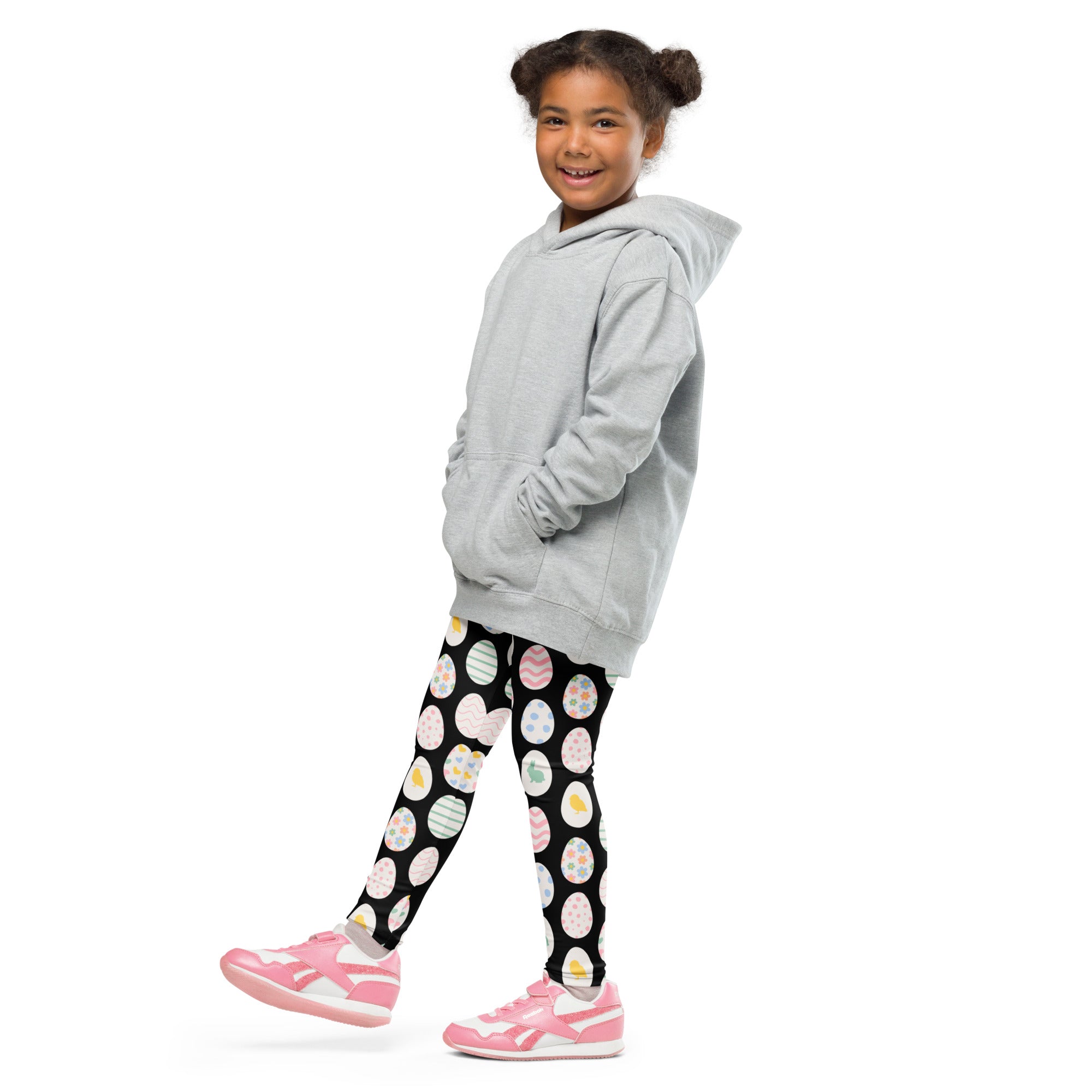 A child wearing black buttery soft leggings with colorful easter egg patterns paired with a light gray hooded sweatshirt