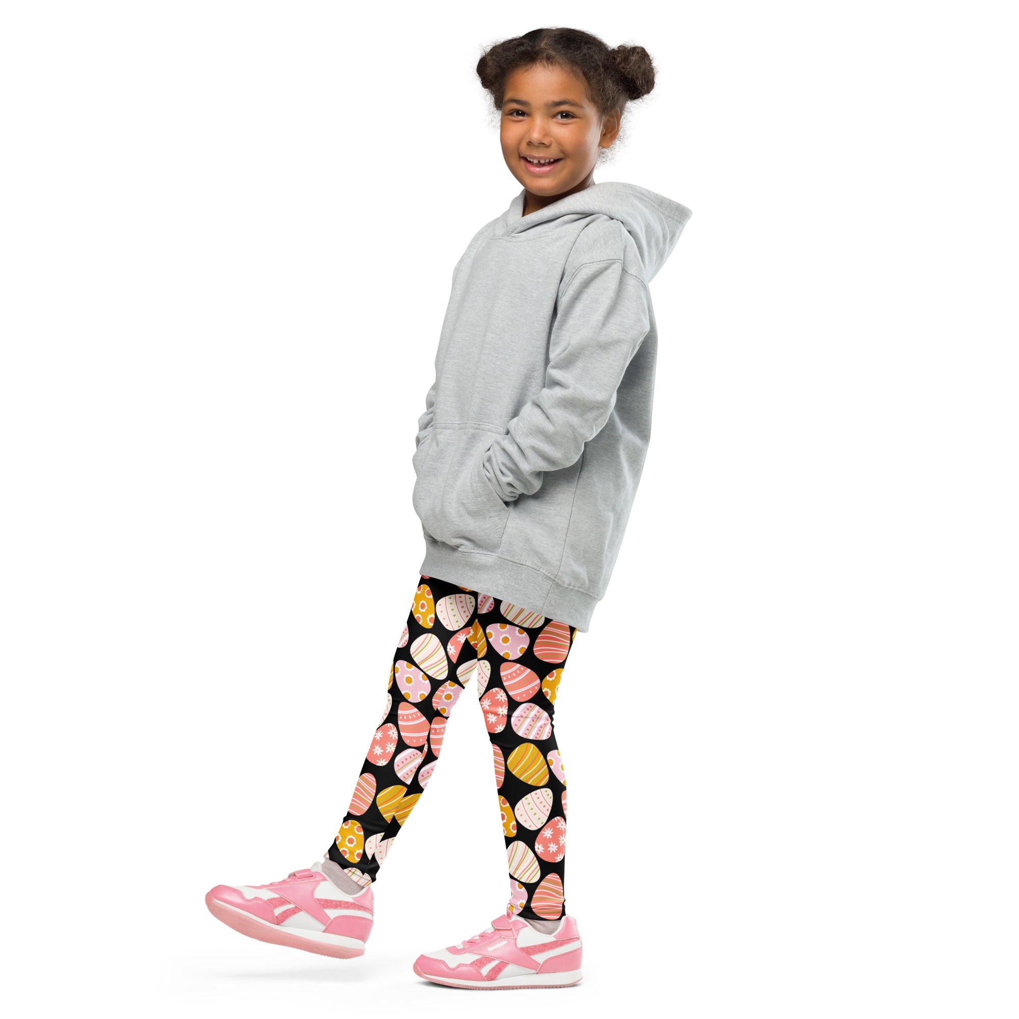 A child wearing light gray hooded sweatshirt and black buttery soft leggings with colorful bold Easter egg patterns