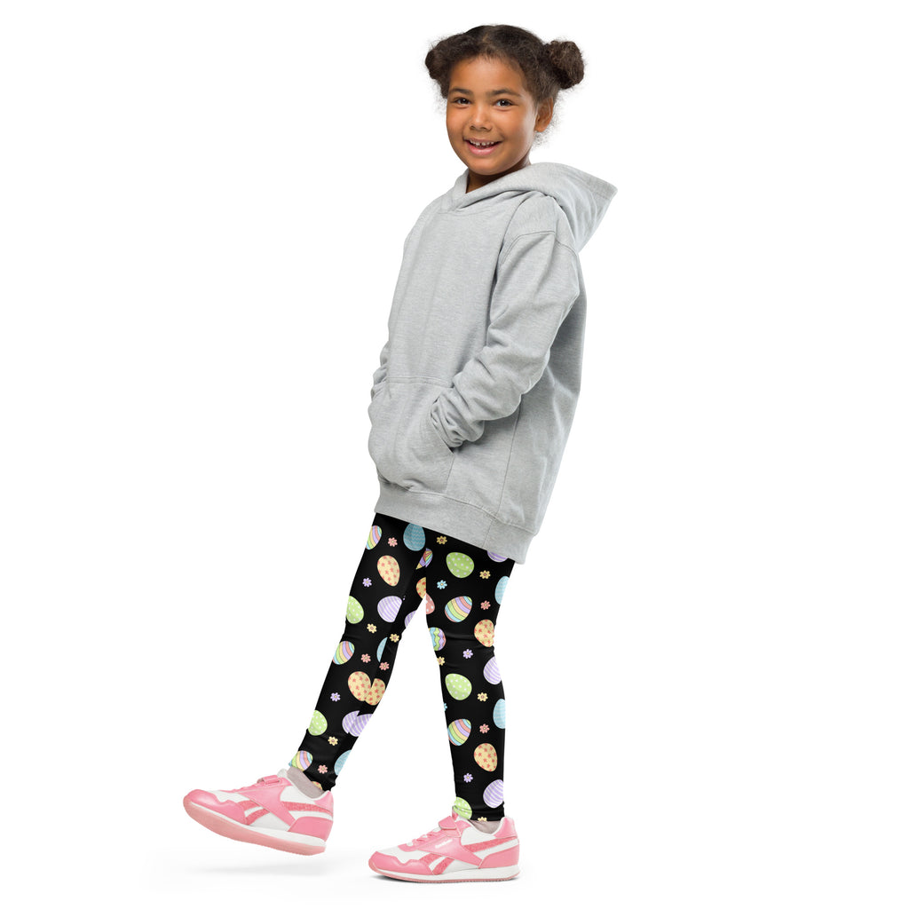 A young girl wearing girls rainbow easter eggs buttery soft leggings with pastel easter egg patterns and pink shoes