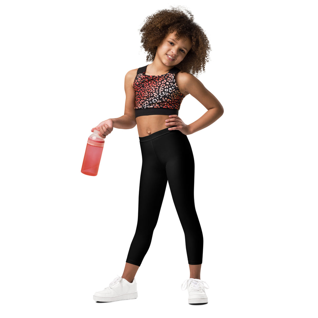 A young girl wearing buttery soft black leggings with leopard print sports bra and white sneakers