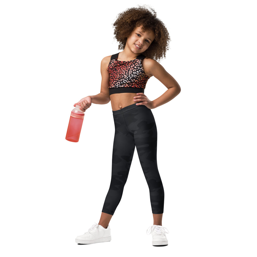 A young girl wearing kids black camouflage buttery soft leggings with leopard print sports bra and white sneakers