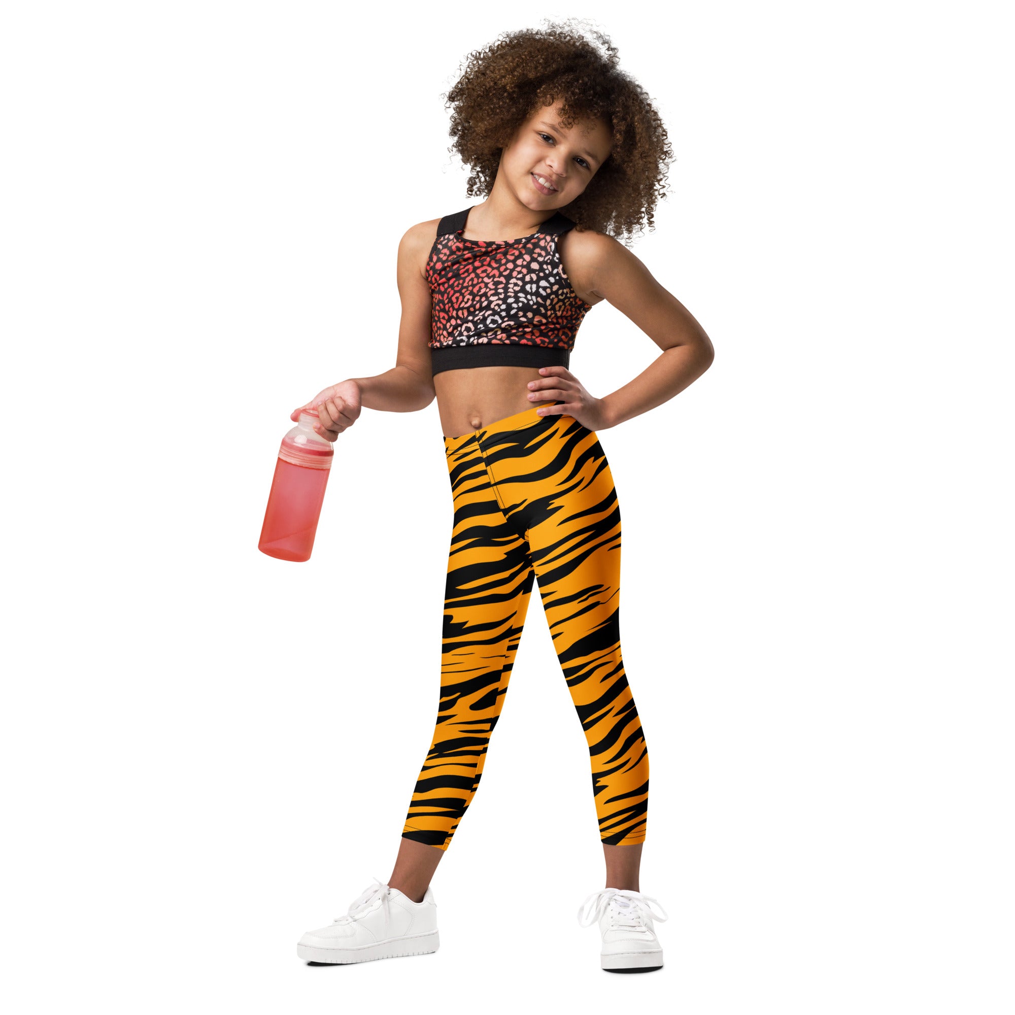 A child wearing kids tiger stripe buttery soft leggings in vibrant orange and black paired with a leopard-print sports bra