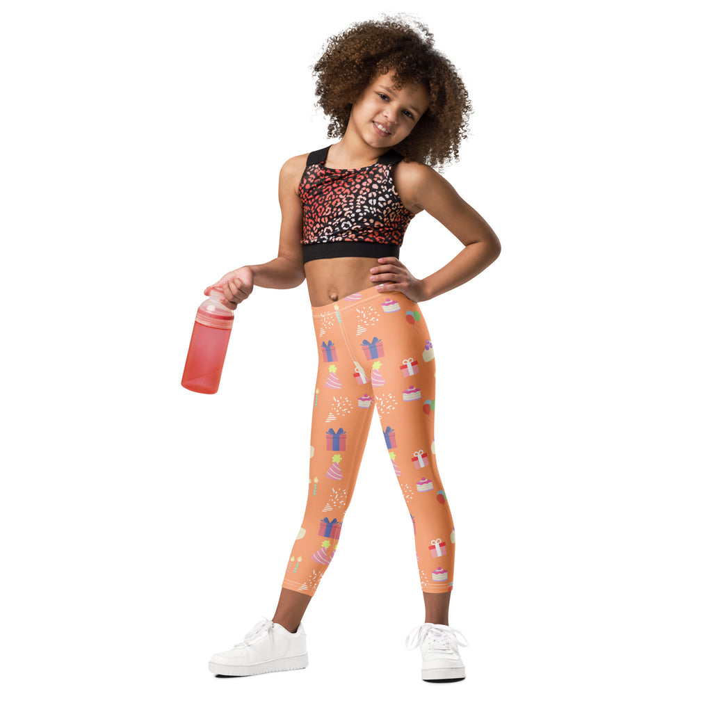 Kids orange buttery soft leggings with playful birthday pattern of cupcakes gifts and party confetti