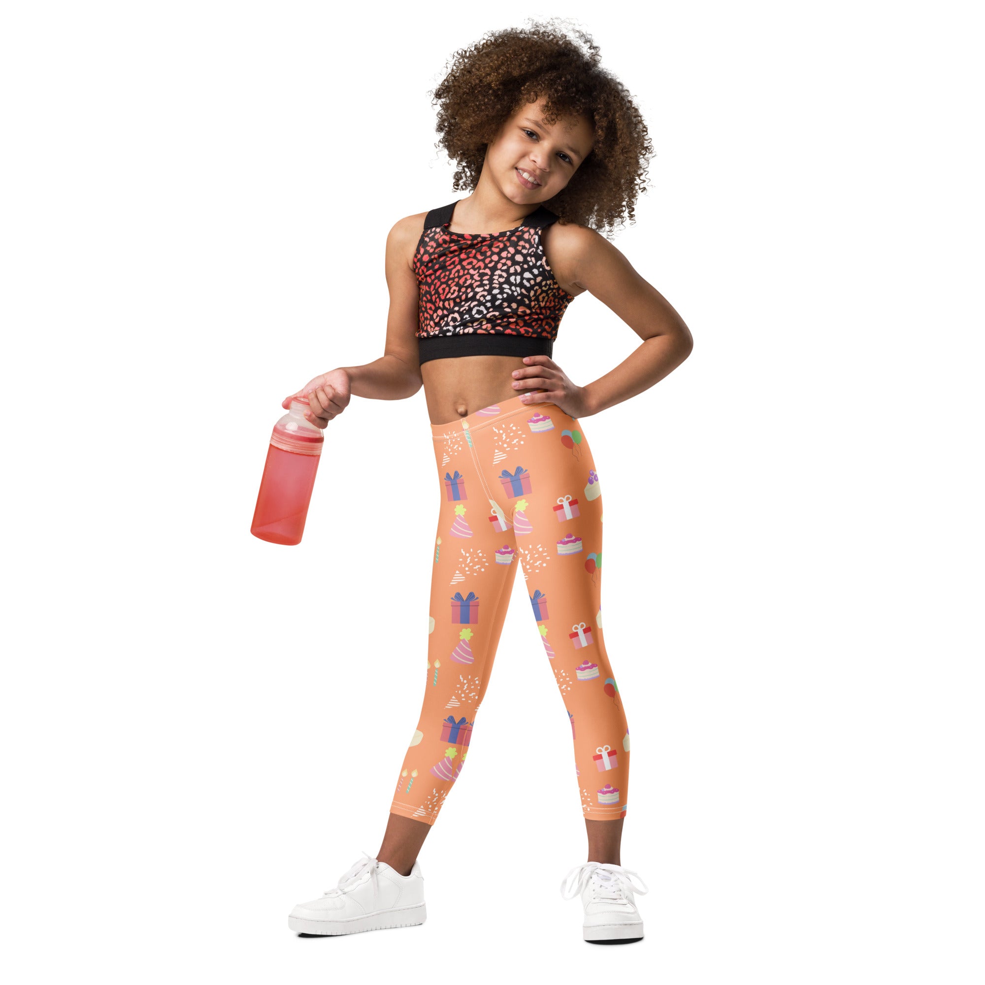 Kids orange buttery soft leggings with playful birthday pattern of cupcakes gifts and party confetti