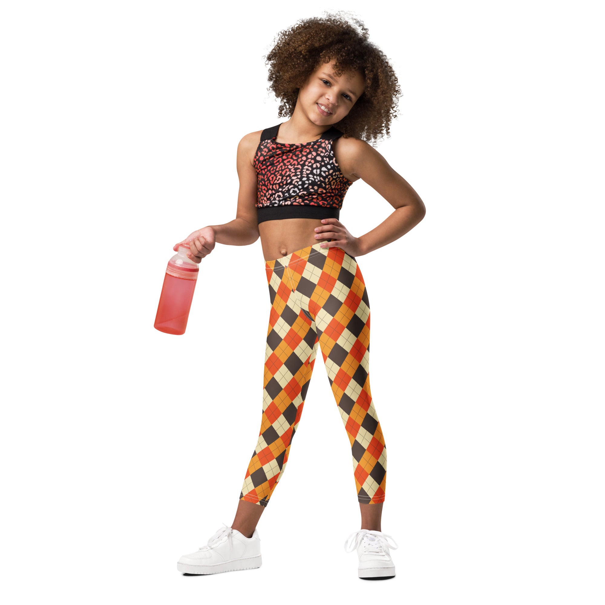 A young girl wearing kids fall argyle buttery soft orange black and beige leggings paired with a leopard-print sports bra