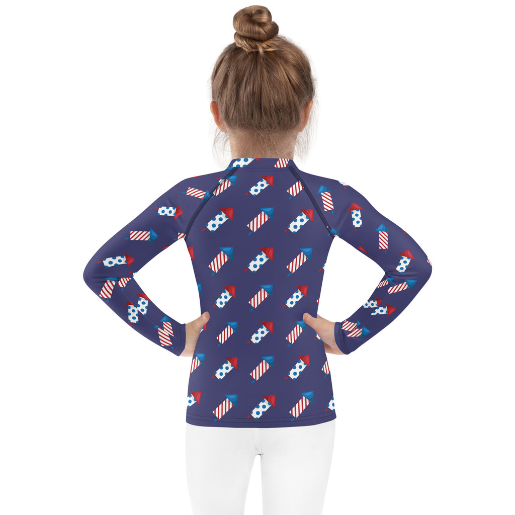 Navy blue kids firework rockets long sleeve rash guard swim shirt with upf 50 plus featuring red white and blue fireworks pattern