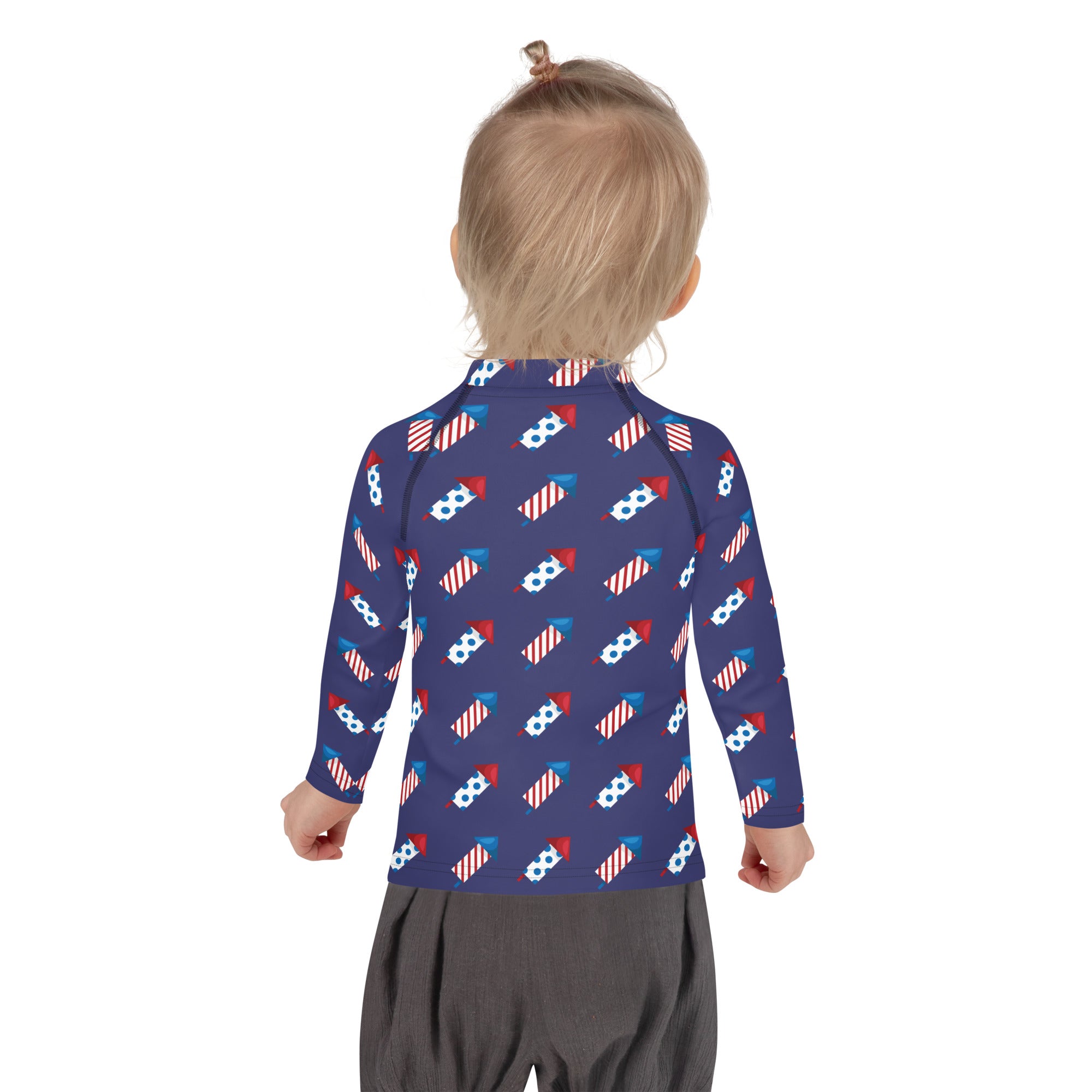 A child wearing a navy blue kids firework rockets long sleeve rash guard swim shirt with UPF 50 plus and fireworks pattern
