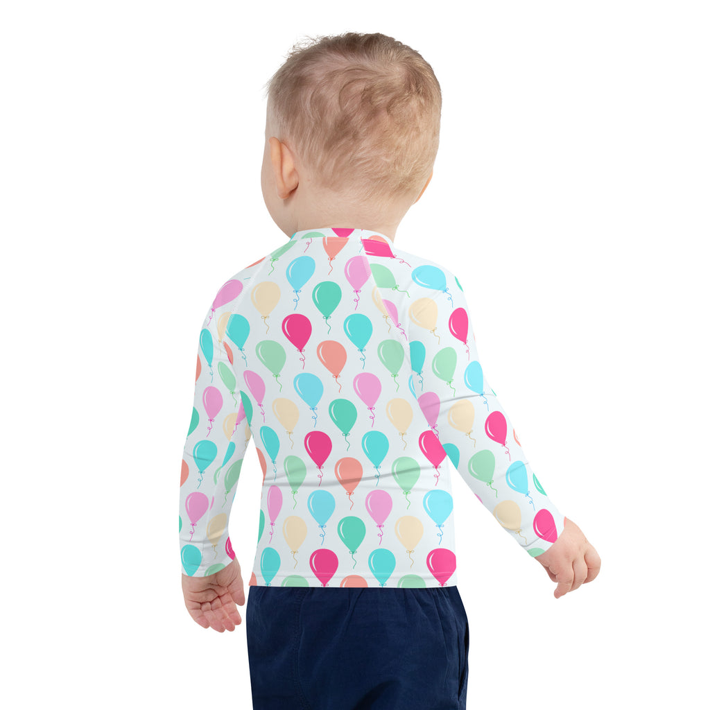 A child wearing a white long sleeve kids birthday balloons rash guard swim shirt with colorful pastel balloons and UPF 50+