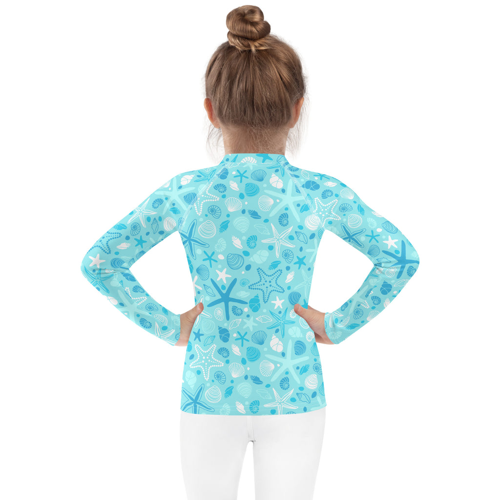 A light blue kids long sleeve rash guard with white and dark blue starfish and seashells and UPF 50+ protection