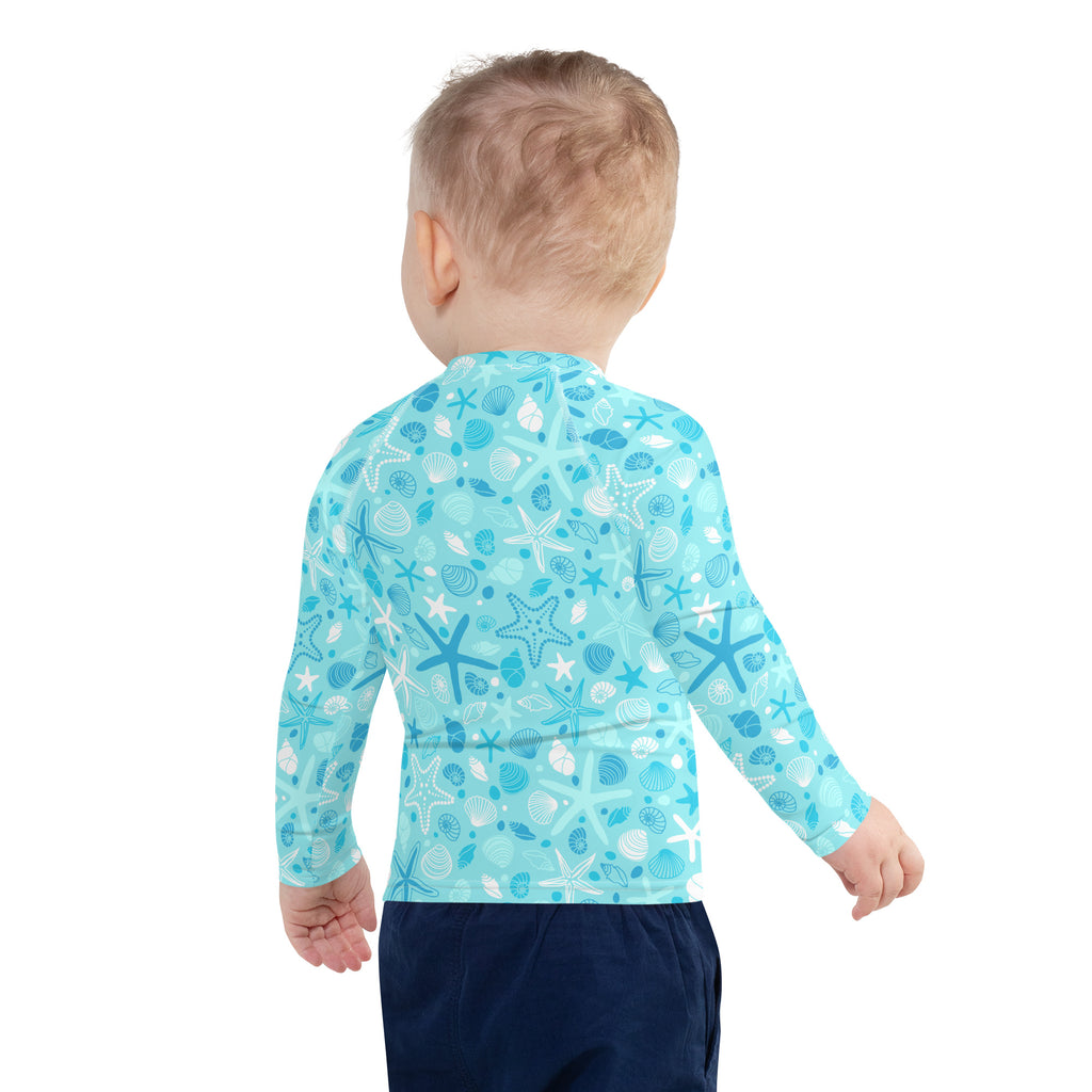 A child wearing a light blue kids starfish and seashell long sleeve rash guard swim shirt with UPF 50+ protection