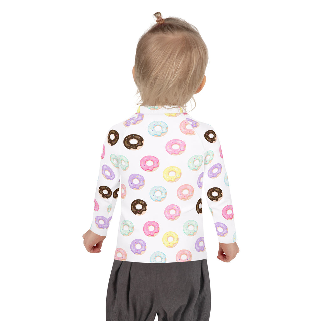 A child wearing a white kids colorful donuts long sleeve rash guard swim shirt with upf 50 plus and pastel prints