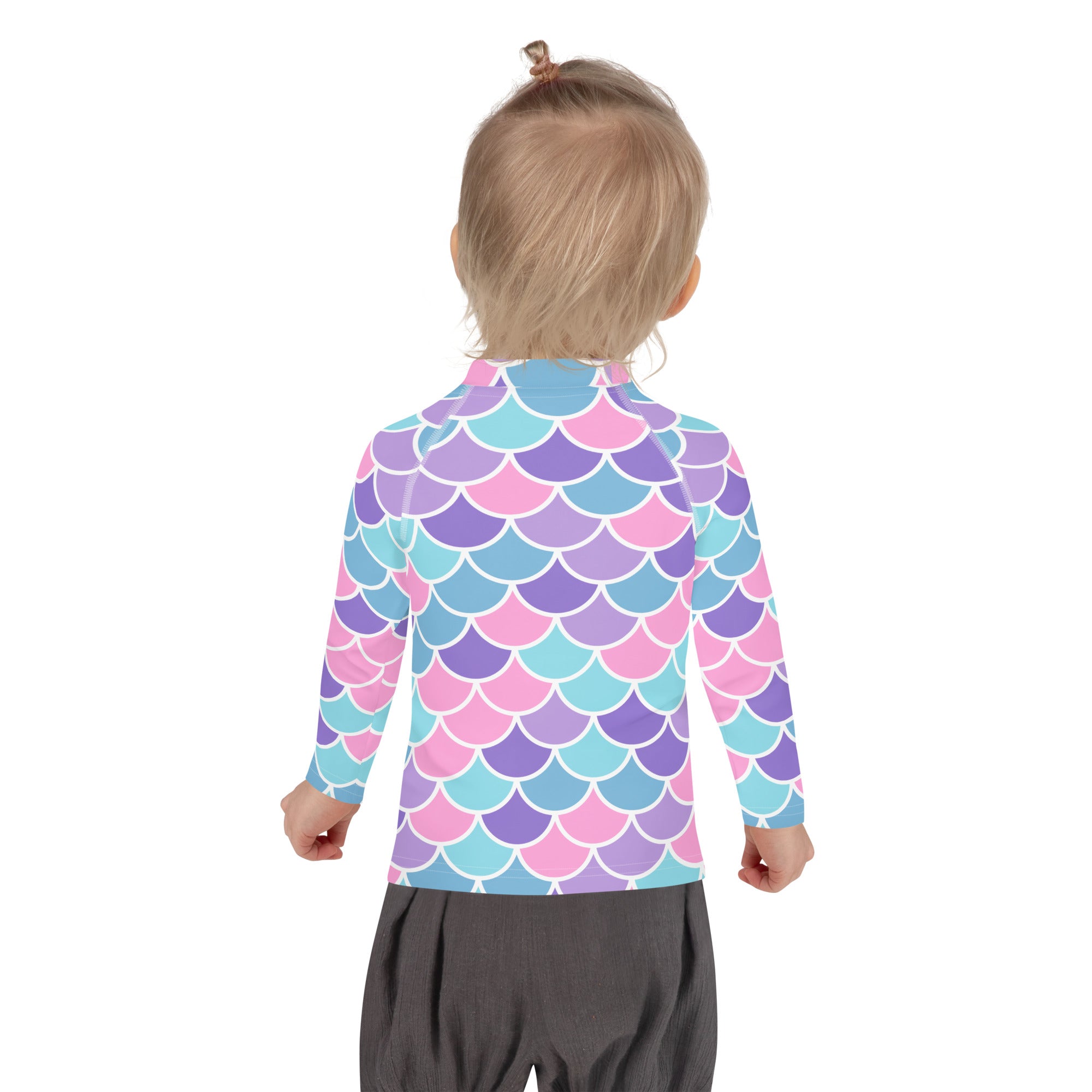 A child wearing a girls pastel mermaid scales long sleeve rash guard swim shirt with vibrant pink purple and light blue scales