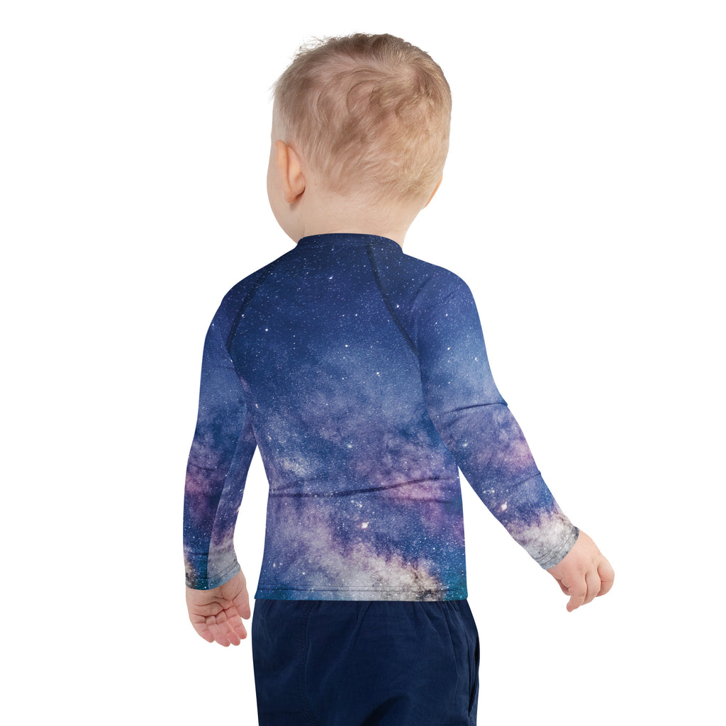 A child wearing a birthday boy realistic galaxy long sleeve rash guard swim shirt with upf 50 in blue and purple