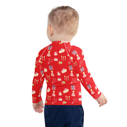 Toddler wearing a red long-sleeve shirt with birthday pattern on a white background