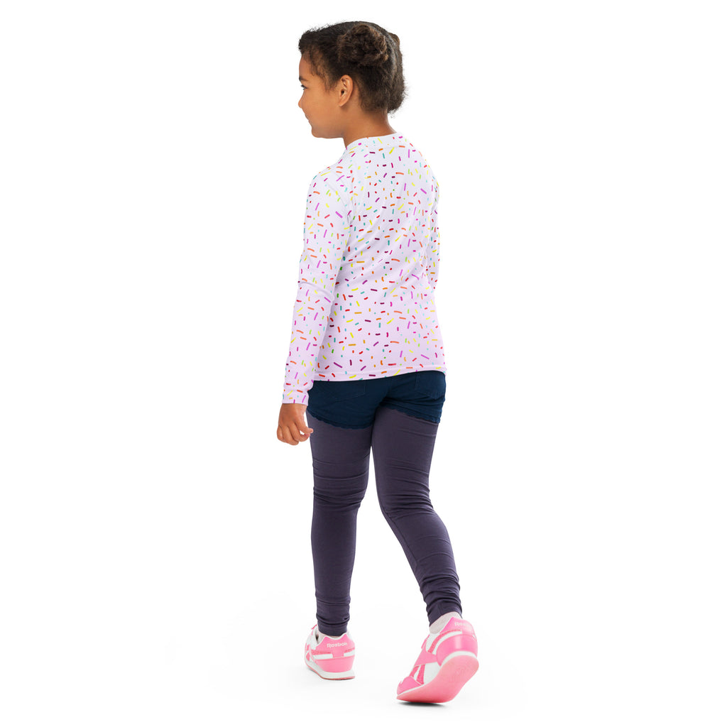 A child wearing a light pink colorful sprinkles birthday girl long sleeve rash guard swim shirt with upf 50+